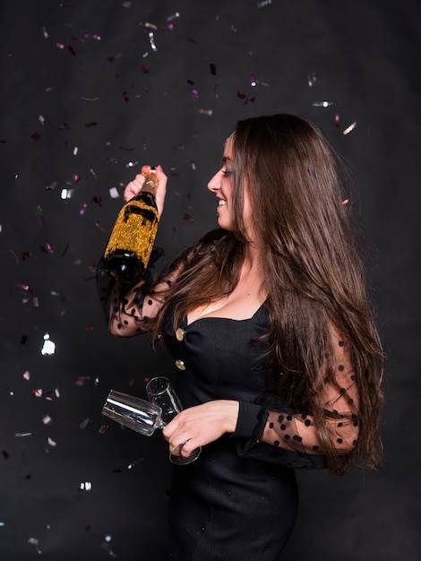 Woman with champagne bottle and glasses under spangles 