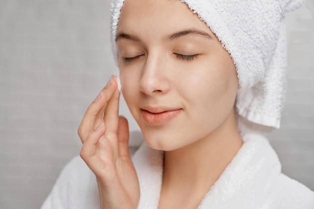 Woman with closed eyes applying moisturizer on face