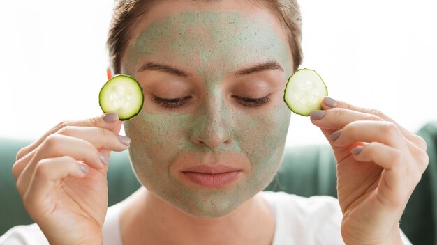 Woman with closed eyes applying slices of cucumber