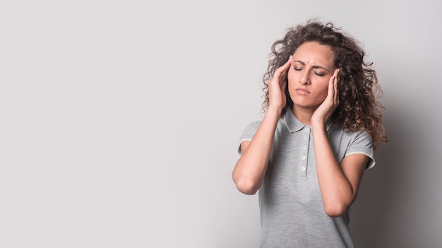 Woman with closed eyes suffering from headache against gray background