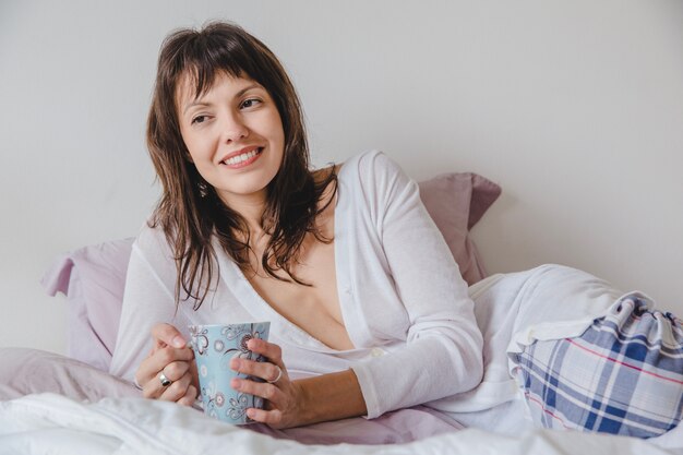 Woman with coffee on bed close up view