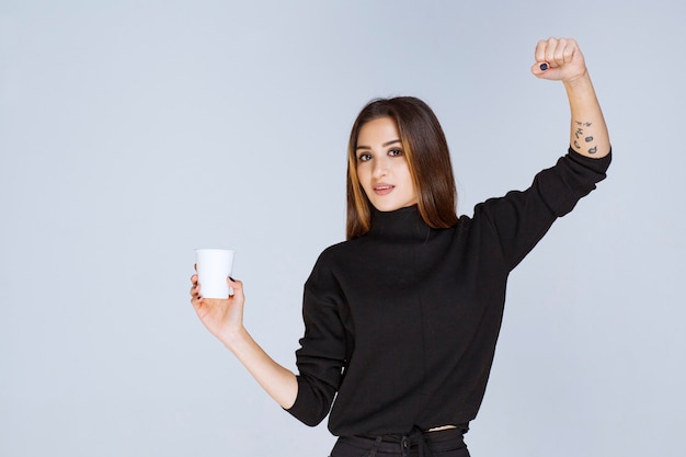 woman with a coffee cup showing her muscles.