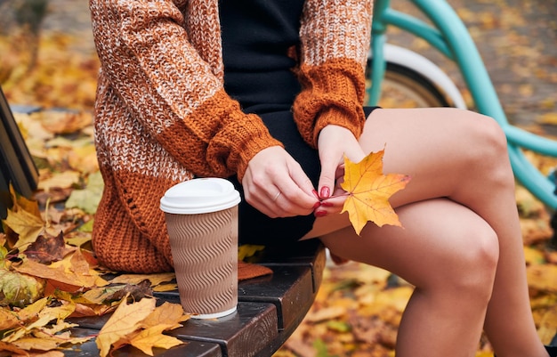 커피를 든 여자가 가을 공원 벤치에서 쉬고 있다