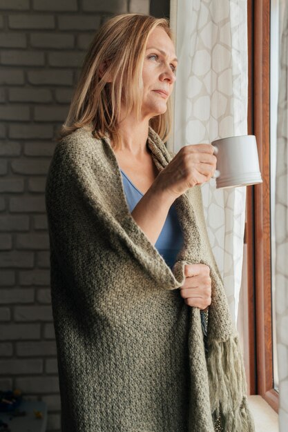 Woman with coffee looking through the window during quarantine