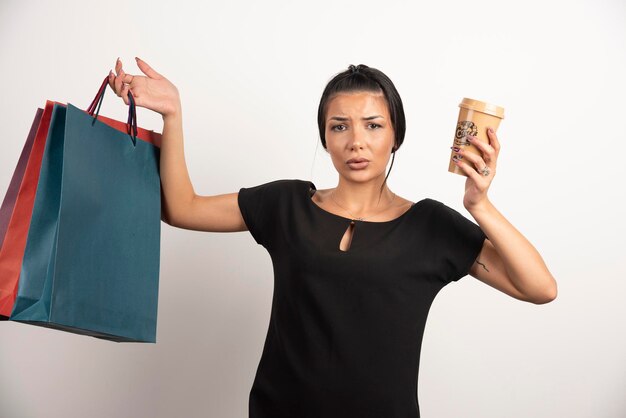 Woman with coffee and shopping bags feeling lost on white wall.