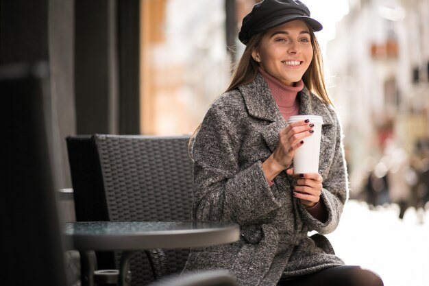 カフェの外に座っているコーヒーを持つ女性