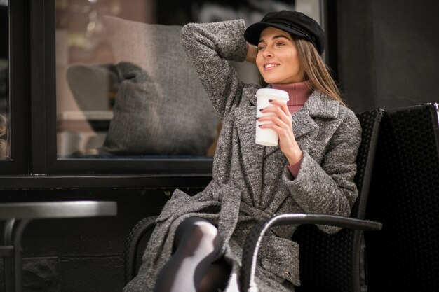 カフェの外に座っているコーヒーを持つ女性