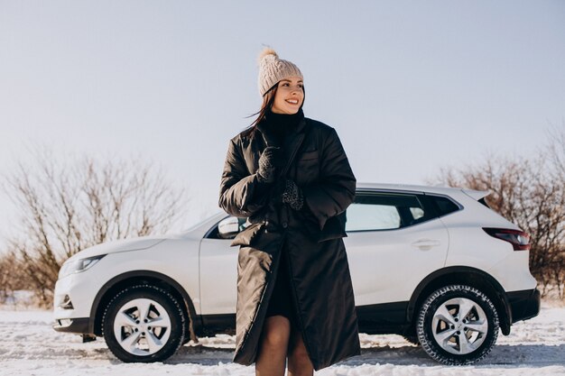 Woman with coffee standing by car in a winter field