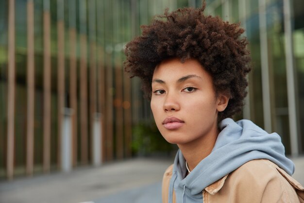 woman with confident face expression dressed in hoodie looks directly at camera poses rests after strolling at city