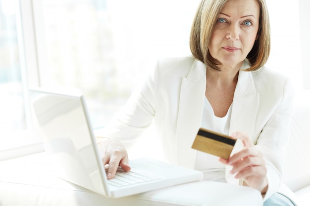 オンラインショッピングのためのクレジットカードやラップトップを持つ女性