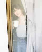 Free photo woman with cup of coffee looking through window