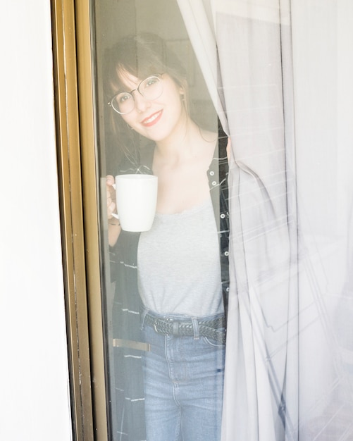 Woman with cup of coffee looking through window