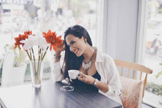 コーヒーのカップと赤の花と花瓶を持つ女性