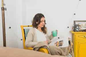 Free photo woman with cup in hand reading a magazine