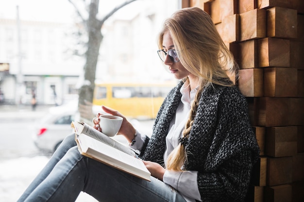 Woman with cup reading near window