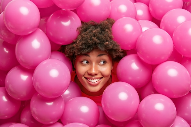 ふさふさした巻き毛の笑顔の女性は、おおむね正しそうに見え、膨らませたヘリウムピンクの風船の周りでお祝いムードのポーズをとっている