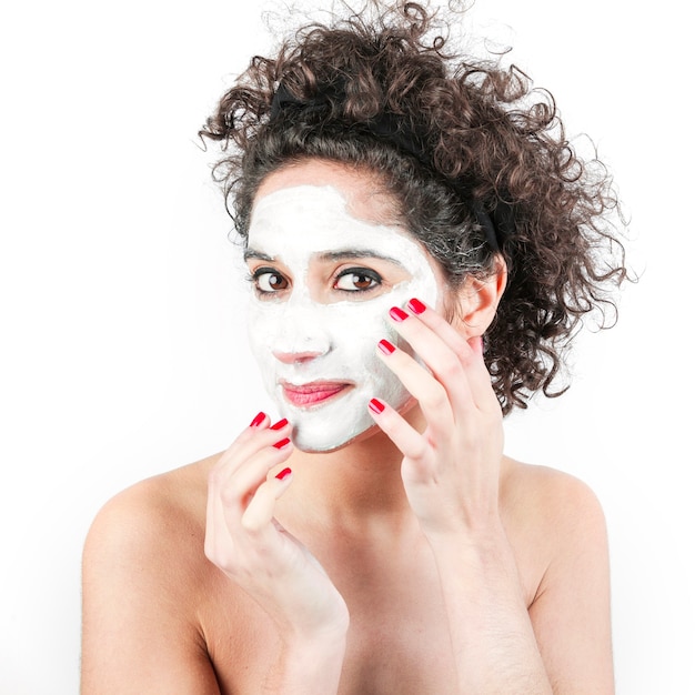 Woman with curly hair applying facial cream on her face against white background