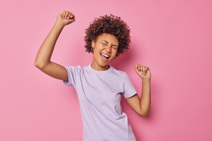 Free Photo woman with curly hair has fun and dances carefree dressed casually isolated on pink enjoys party and favorite music isolated on pink. people and emotions