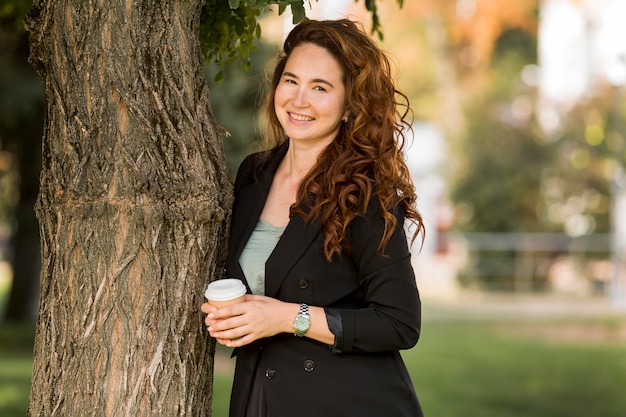 Woman with curly hair posing next to a tree