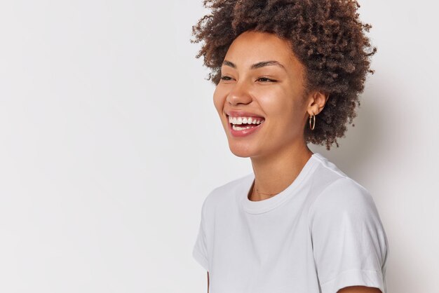 巻き毛の笑顔の女性は、広告コンテンツの白いコピースペースに隔離されたカジュアルなTシャツを着た白い歯を広く示しています。幸せな感情
