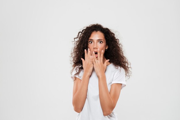 Woman with curly hair standing and covering mouth with hands