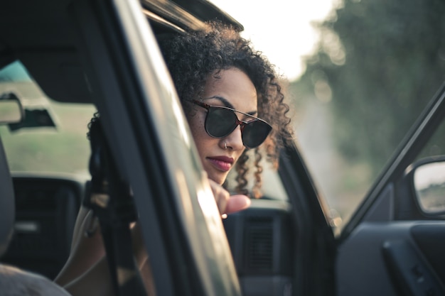 車の外を見ている巻き毛とサングラスを持つ女性