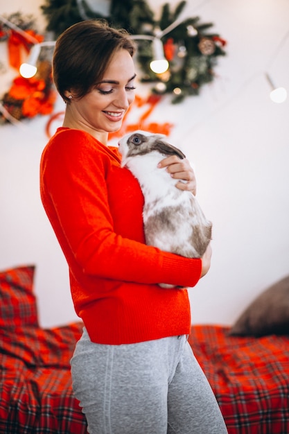 Woman with cute bunny by Christmas tree