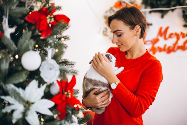 Woman with cute bunny by Christmas tree