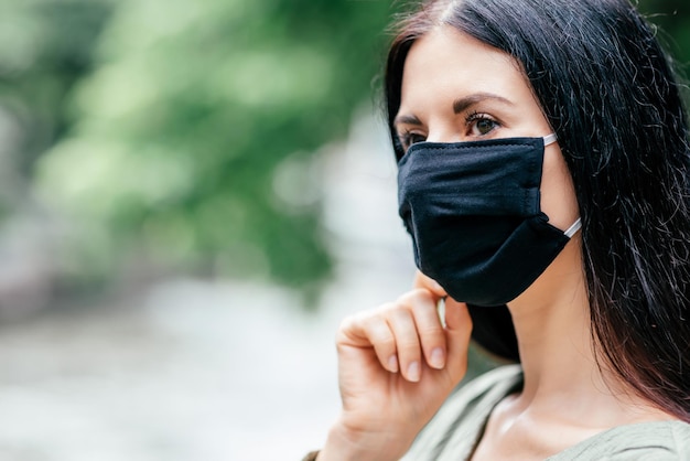 woman with dark hair, looking away, while wearing medical mask, standing outdoors. Safety, coronavirus, pandemic concept