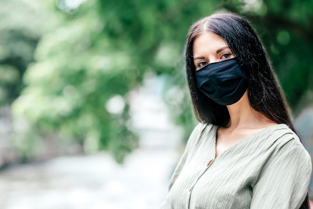 黒髪の女性、カメラを見て、医療用マスクを着用し、屋外に立っています。安全性、コロナウイルス、パンデミックの概念