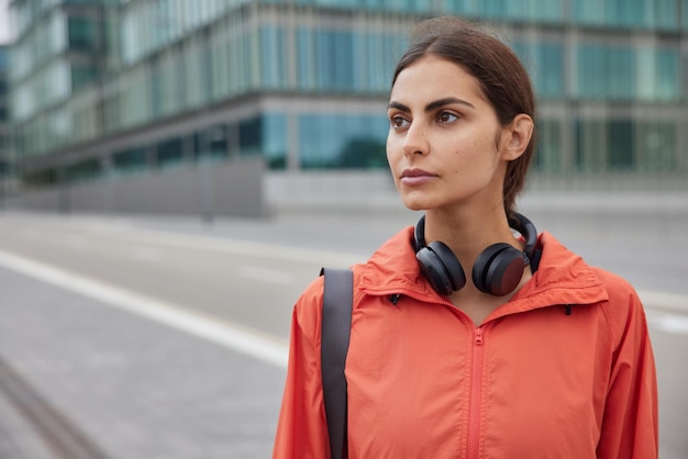 woman with dark hair strolls against urban setting with sport facilities leads active lifestyle focused forward into distance thinks about plans for day