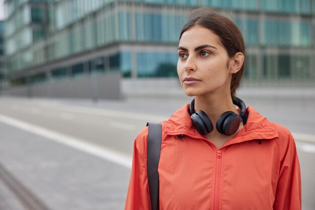 woman with dark hair strolls against urban setting with sport facilities leads active lifestyle focused forward into distance thinks about plans for day