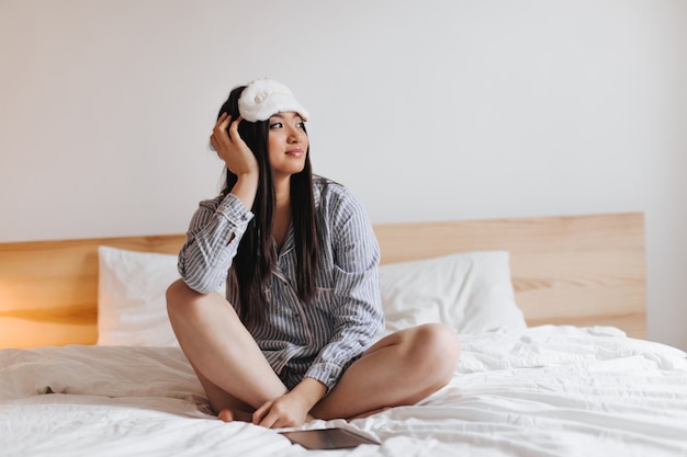 woman with dark long hair is resting on white bed