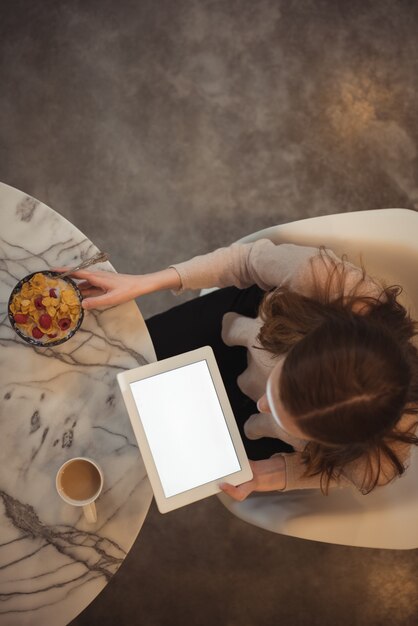 Woman with digital tablet having breakfast at home