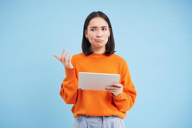 Woman with digital tablet looks confused cant understand smth on her gadget stands puzzled against b