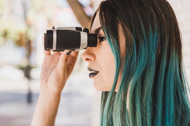 A woman with dyed hair looking through binocular