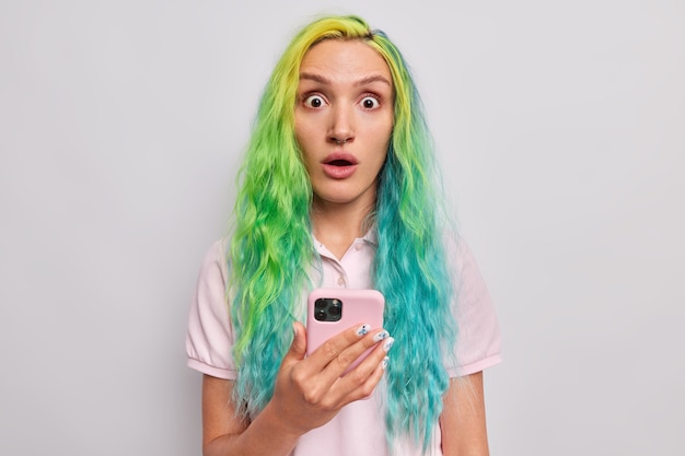  woman with dyed haor receives unexpected notification on cellular cannot believe her eyes reacts emotionally to mobile offer wears t shirt isolated on grey 