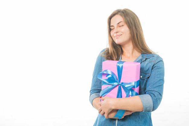 Woman with eyes closed holding birthday gift on white background