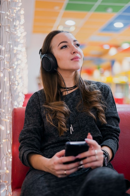 クリスマスライトの近くの携帯電話を保持しているヘッドフォンを着て目を閉じて女性