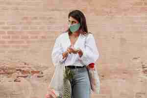 Foto gratuita donna con maschera facciale e sacchetti della spesa utilizzando disinfettante per le mani