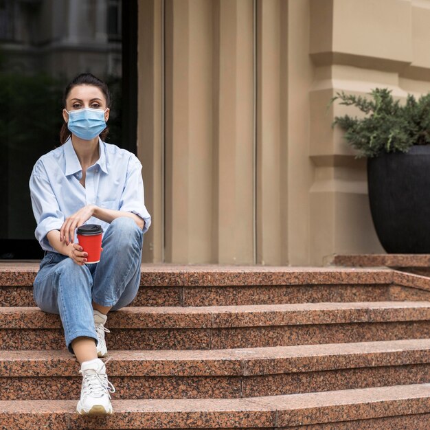 Woman with face mask holding a cup of coffee with copy space