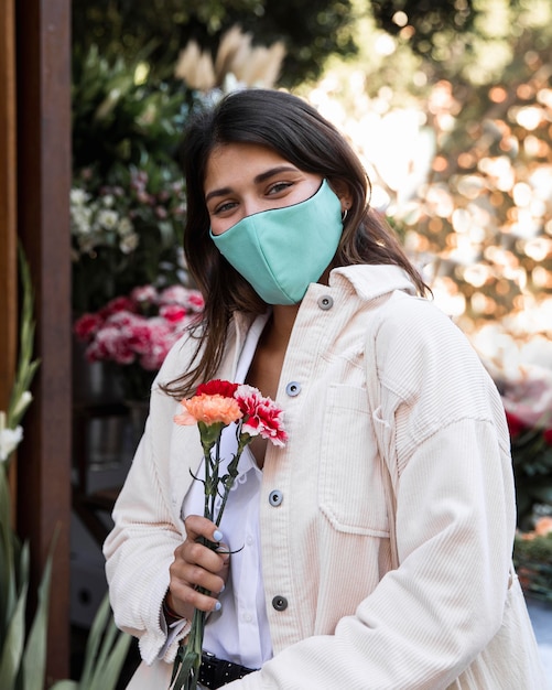 Foto gratuita donna con maschera facciale in posa all'aperto con fiori