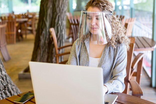 Woman with face protection while working on laptop
