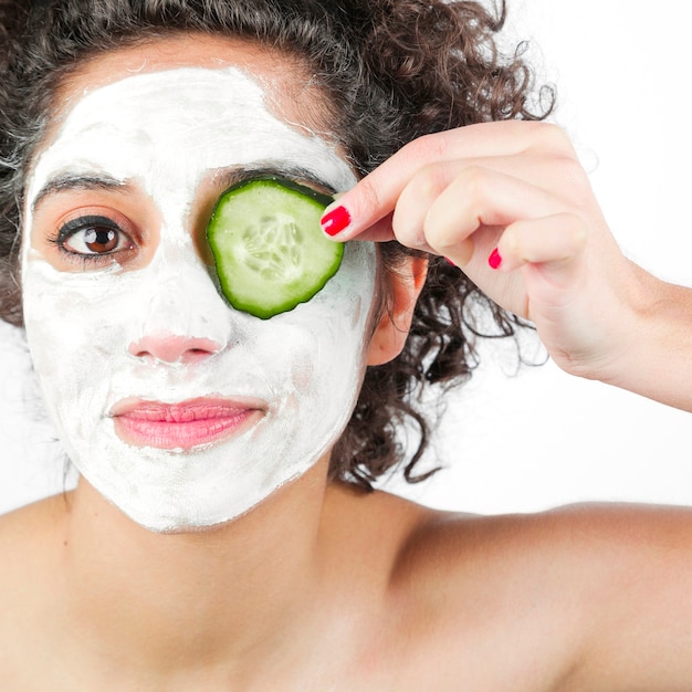 Woman with facial mask applying cucumber slice over one eye