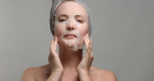 Woman with a facial sheet mask on makes herself a facial a massage