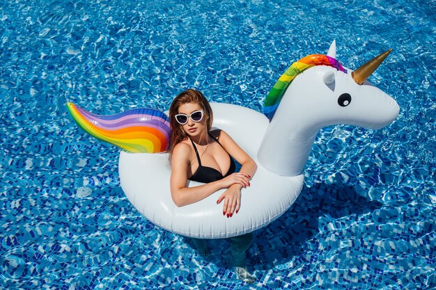 Woman with a figure in black swimsuit and sunglasses is resting in swimming pool