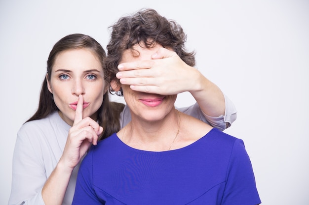 Woman with finger on lips covering mothers eyes