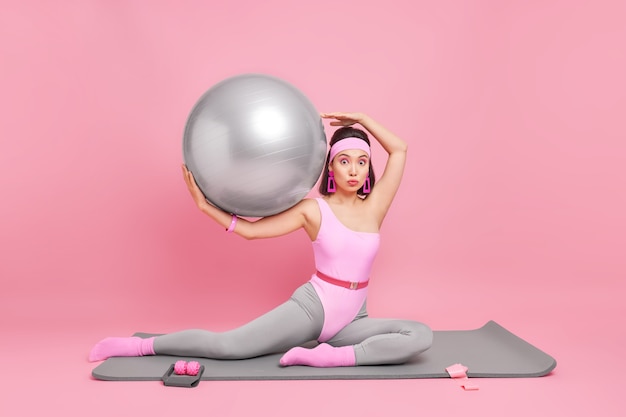 woman with fit body does aerobics exercises being fitness instructor works at training centre holds pilates ball dressed in activewear 