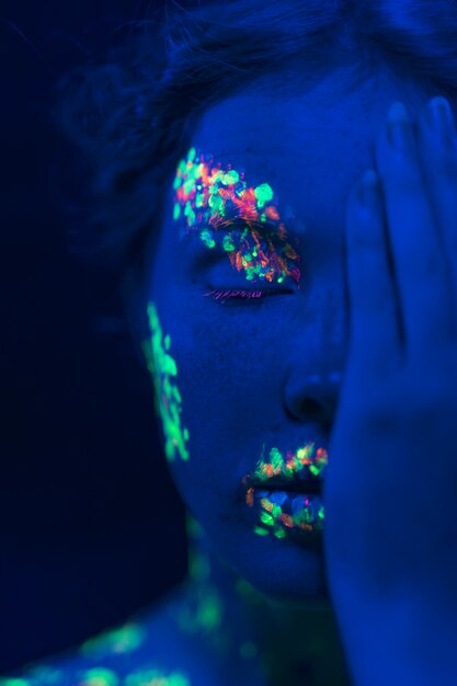 Woman with fluorescent make-up and hand on her face