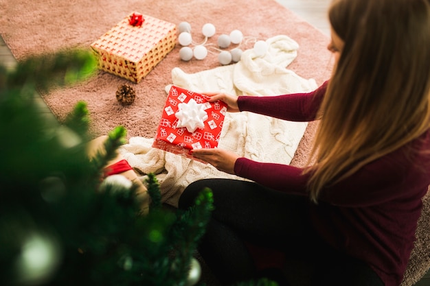 Woman with gift box near snag, fairy lights and Christmas tree 